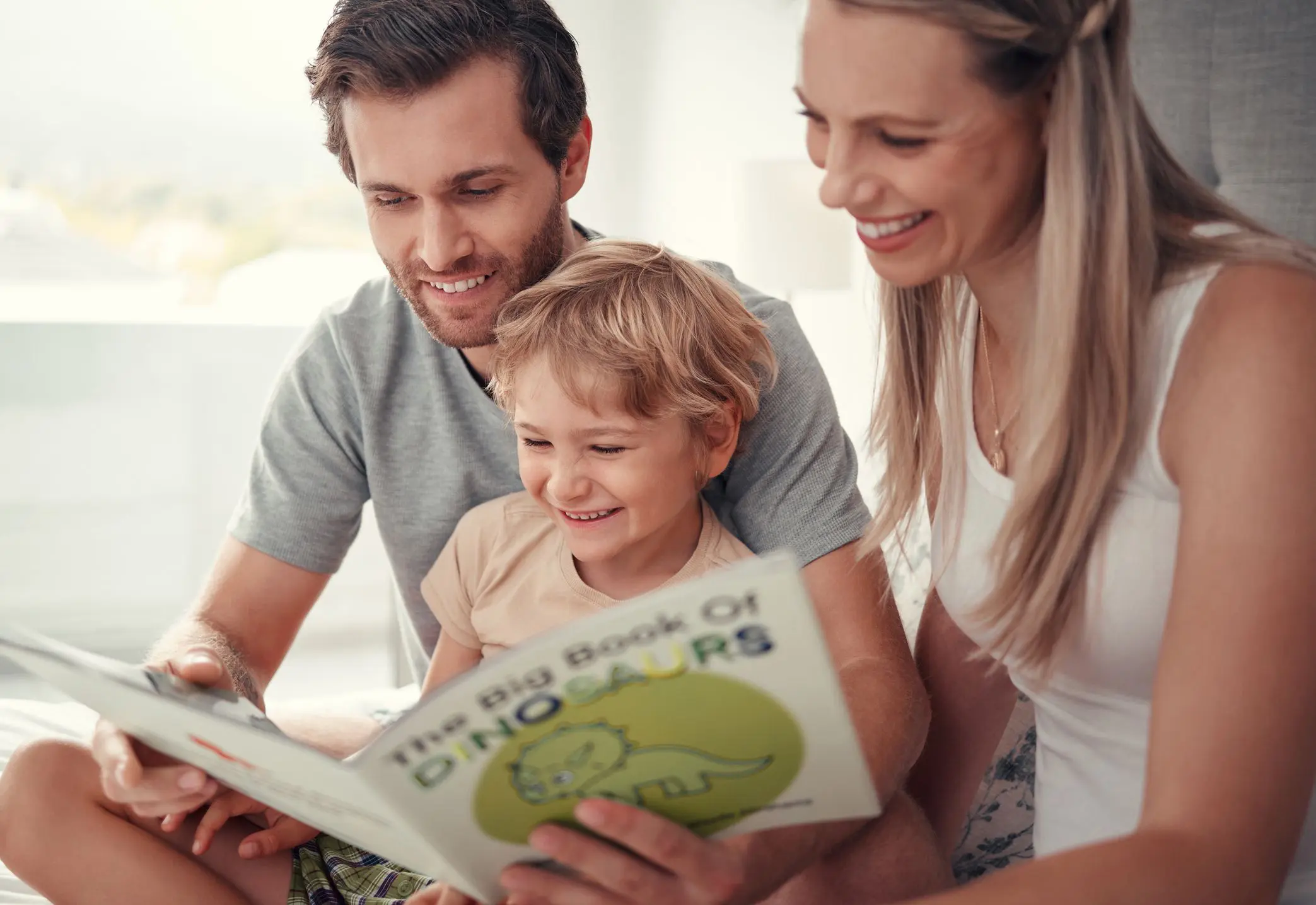 Family reading dinosaur book together, smiling.