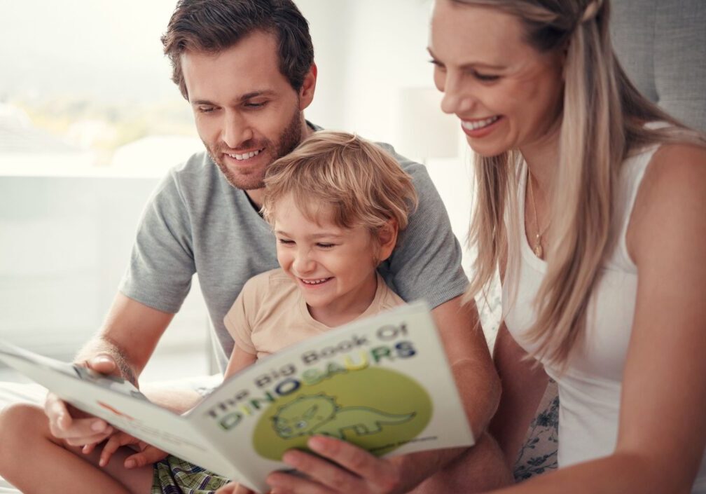 Family reading dinosaur book together, smiling.